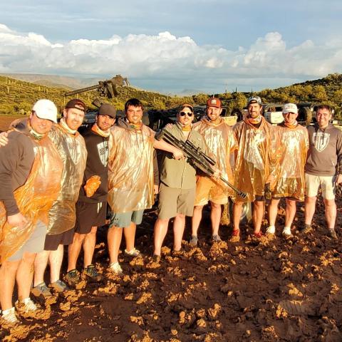 Group of men in orange ponchos standing on muddy ground with a large vehicle in the background.