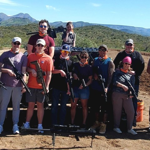 Group of people holding rifles posing outdoors with a mountainous landscape in the background.