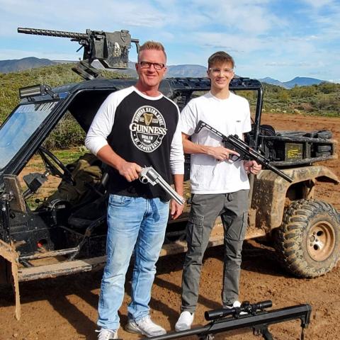 Two people holding guns standing by an off-road vehicle with a mounted gun.