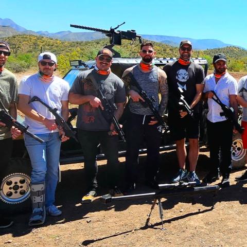 Group of men standing in front of a vehicle with guns in a desert setting.