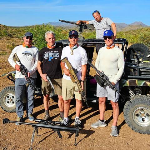 Five men with firearms posing by an off-road vehicle in a desert landscape.