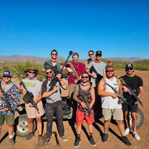 Group of men with rifles posing in desert landscape on a sunny day.