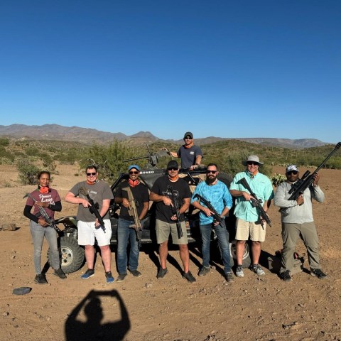 Group of eight people holding rifles in a desert landscape.