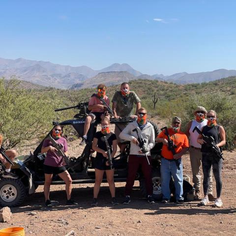 Group of people with paintball gear posing by a cart in a desert landscape.