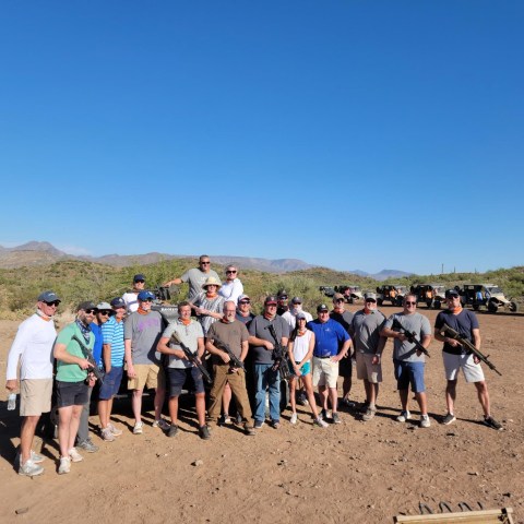Group of people posing in a desert landscape with off-road vehicles in the background.