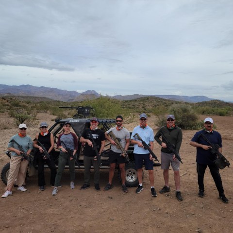 Group of people posing with equipment in a desert landscape under cloudy sky.