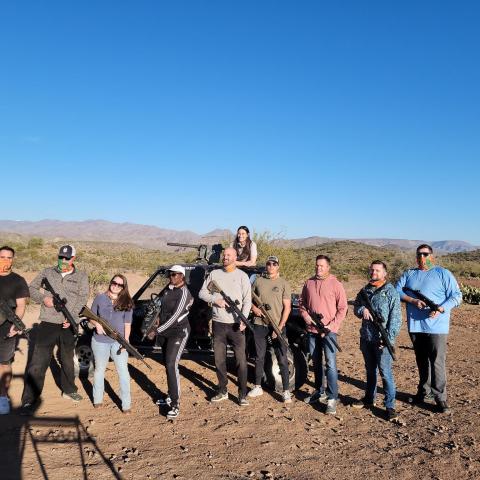 Group of ten people with rifles posing in a desert landscape during the day.