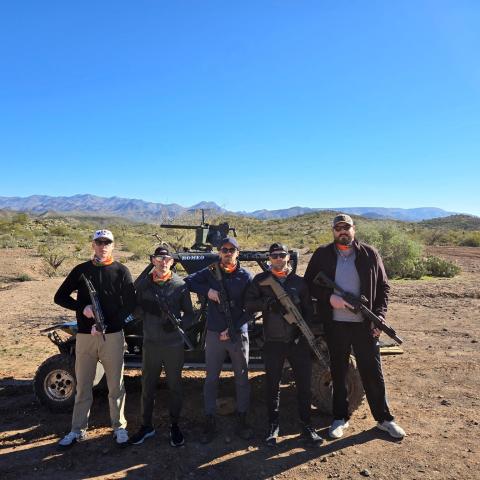 Five people with firearms pose in front of a buggy in a desert landscape.