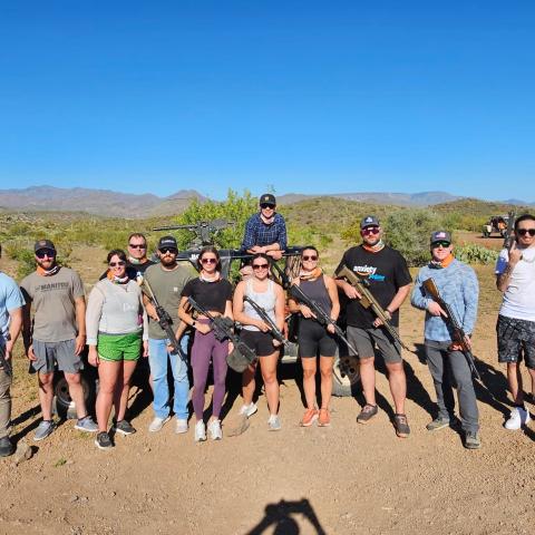 Group of people holding guns outdoors on a sunny day.