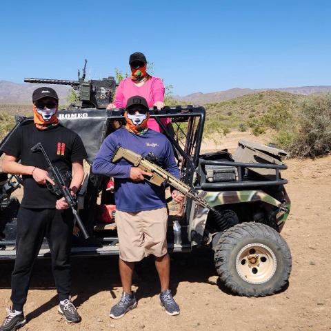 Three people with masks stand by an off-road vehicle in a desert landscape.