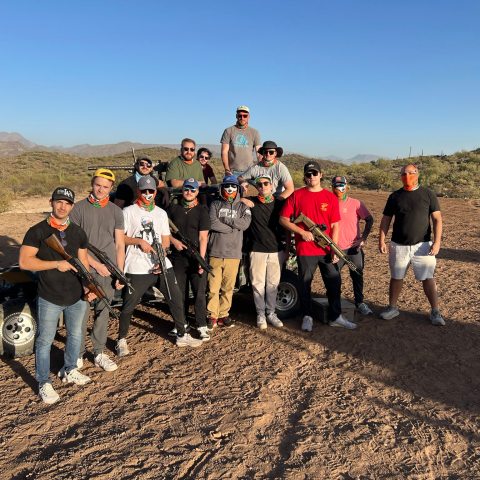 Group of people with guns posing in a desert landscape with clear sky.