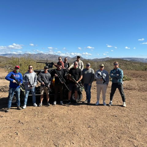 Group of people with rifles standing in a desert landscape with mountains in the background.