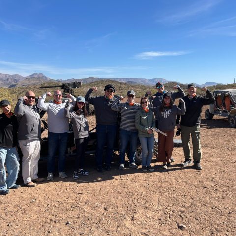 Group of people posing with raised fists near off-road vehicles in a desert landscape.