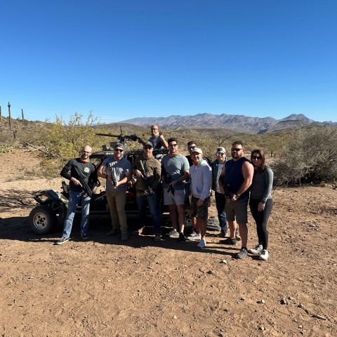 Group of people posing in a desert landscape with a vehicle under clear blue sky.