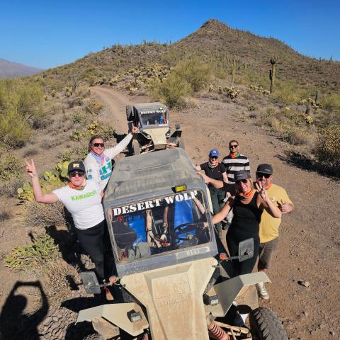 Group of people posing with off-road vehicles in a desert landscape under a clear blue sky.