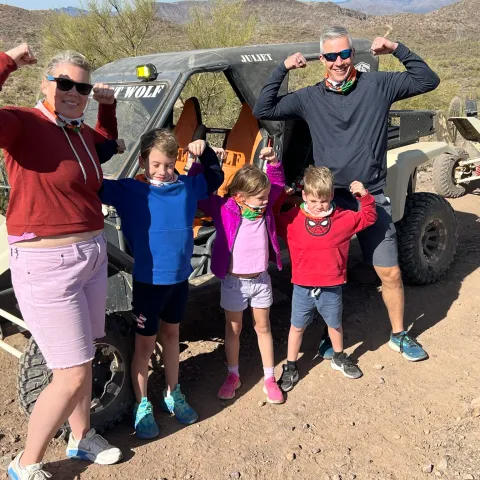 Family flexes muscles beside off-road vehicles in desert landscape.