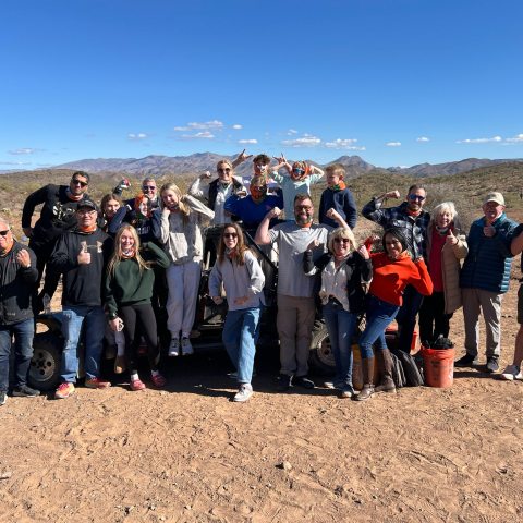 Group of people posing outdoors on a sunny day in a desert landscape.
