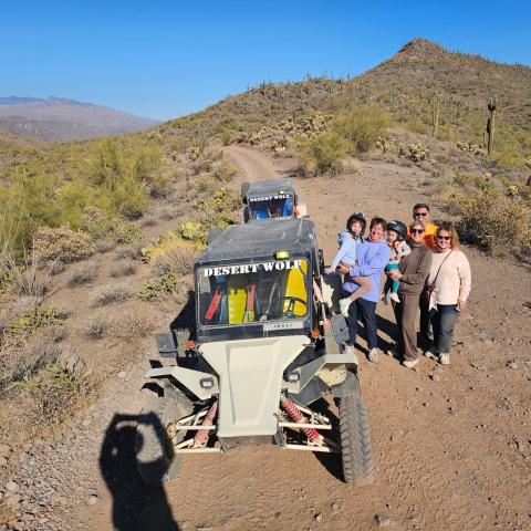 Group of six near off-road vehicle labeled 'Desert Wolf' on a desert trail with cacti and hills in the background.