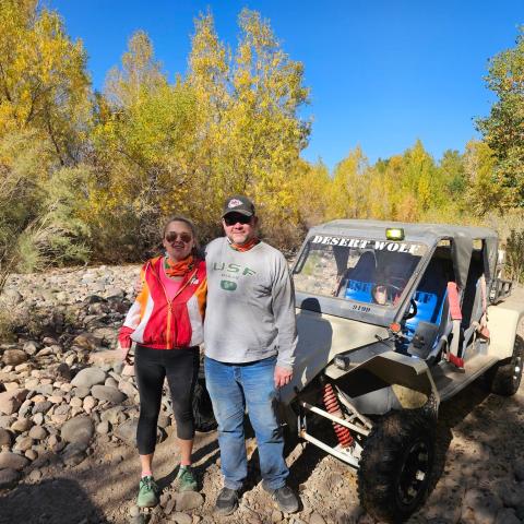 Two people smiling next to an off-road vehicle in a rocky, wooded area.