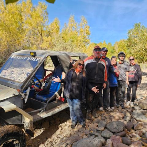 Group of people posing next to an off-road vehicle surrounded by trees and rocks.