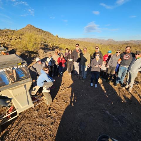 Group of people standing on a desert trail next to off-road vehicles under a clear sky.