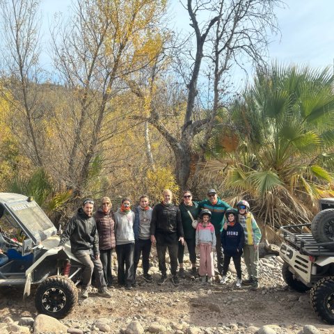 Group of people posing between two off-road vehicles in a forested area with autumn trees.
