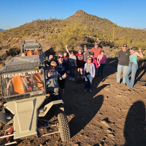 Group posing near off-road vehicles in a desert landscape with clear blue sky.