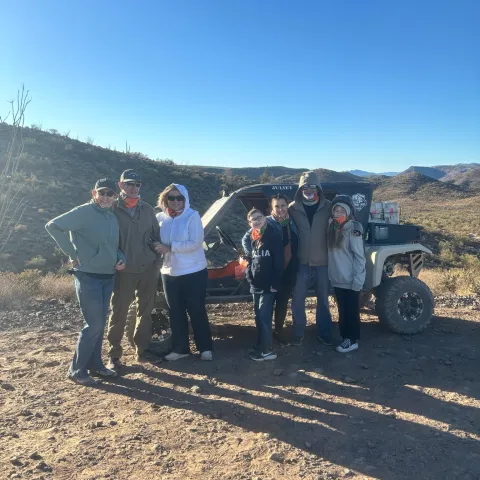 Group of people in jackets standing by an off-road vehicle in a desert landscape.