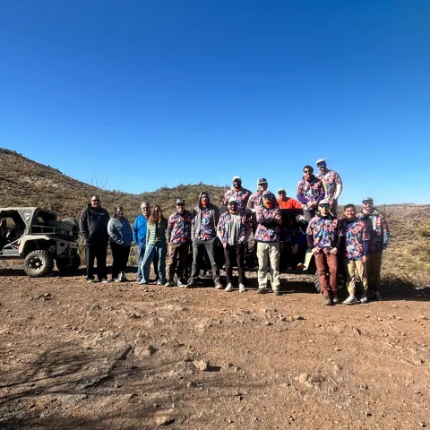 Group poses with a UTV in a desert landscape under a clear blue sky.