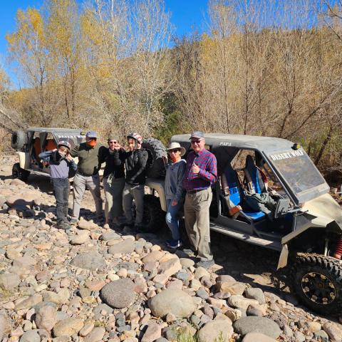 Group of people posing with two off-road vehicles on a rocky terrain.