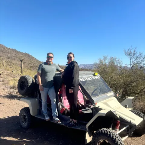 Two people posing on a dune buggy in a desert landscape with clear blue sky.