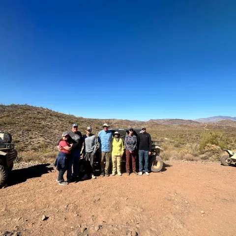 Group of people standing on a dirt path with desert landscape and blue sky.