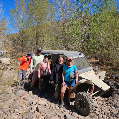 Group of five people posing with dune buggies in a rocky, wooded area.