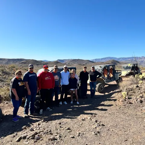 Group of people standing by off-road vehicles in a desert landscape.