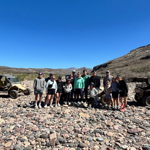 Group of people standing on rocky terrain with off-road vehicles under a clear blue sky.