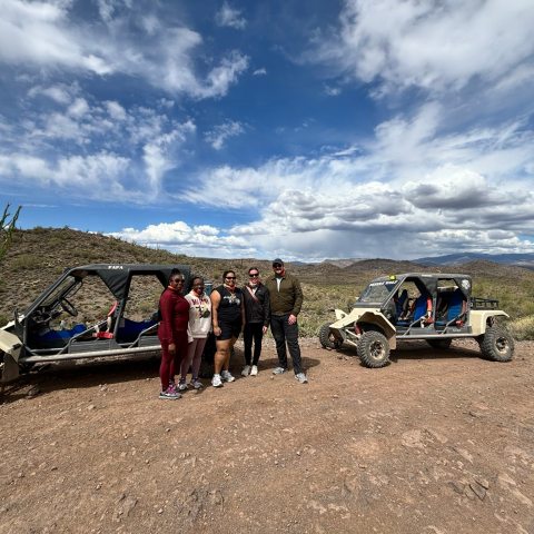 Group of people standing between two off-road buggies in a desert landscape with cloudy sky.