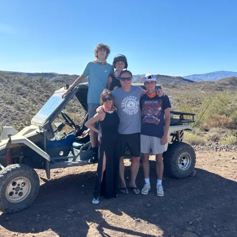 Family of five posing in front of an off-road vehicle in a desert landscape.