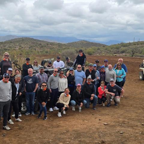 Group posing in desert landscape with off-road vehicles in the background.