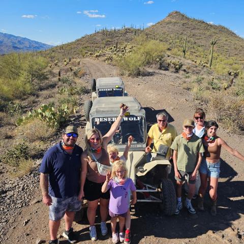 Group posing with a Desert Wolf off-road vehicle in a desert landscape with cacti and hills.