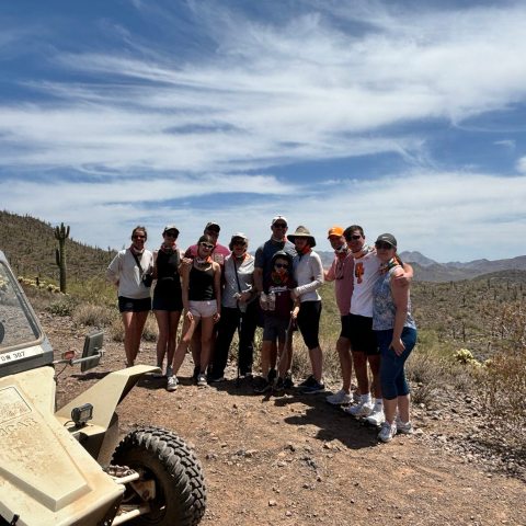 Group of smiling guests on a Scottsdale & Phoenix Sonoran Desert ATV tour with Desert Wolf Tours, standing beside their Tomcar with no helmets or goggles.